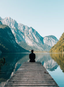 A man sitting on a dock in front of mountains. by Chasing the Sun Vacations