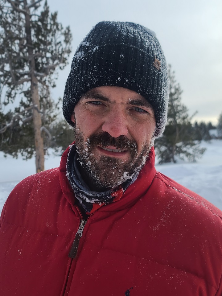 A man wearing a red jacket and beanie in the snow. by Chasing the Sun Vacations