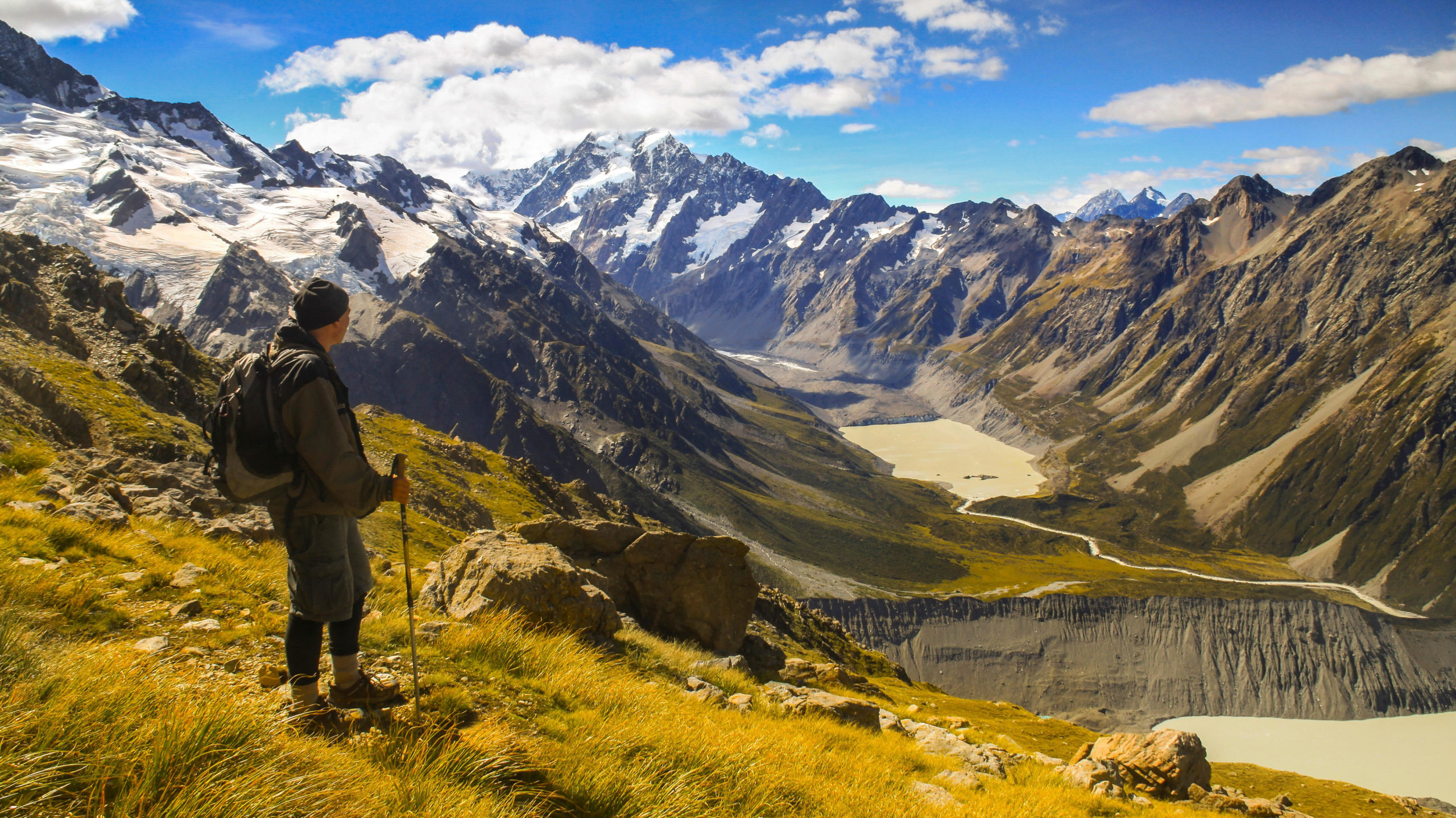 A man standing on the side of a mountain overlooking a lake, contemplating his upcoming cruise adventure. by Chasing the Sun Vacations