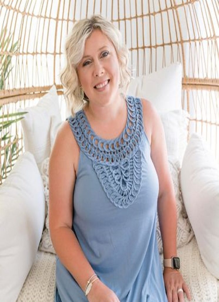 A woman in a blue crochet dress sitting on a wicker chair at an all-inclusive resort recommended by her travel advisor. by Chasing the Sun Vacations