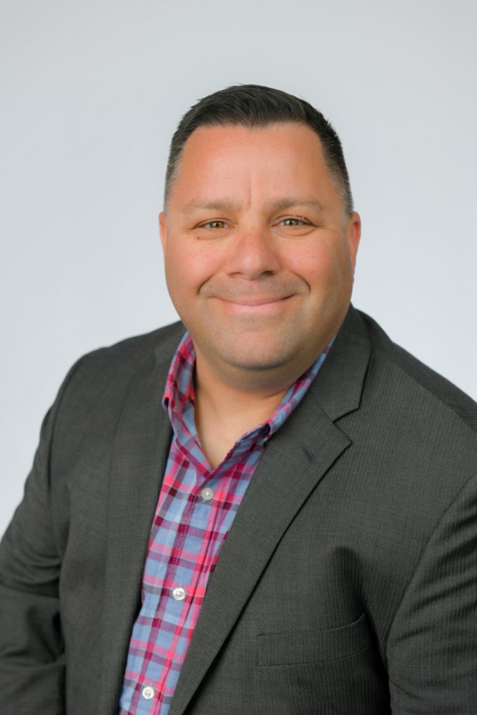 A man in a gray suit smiling for the camera, representing a professional travel agent ready to book your all-inclusive cruise. by Chasing the Sun Vacations