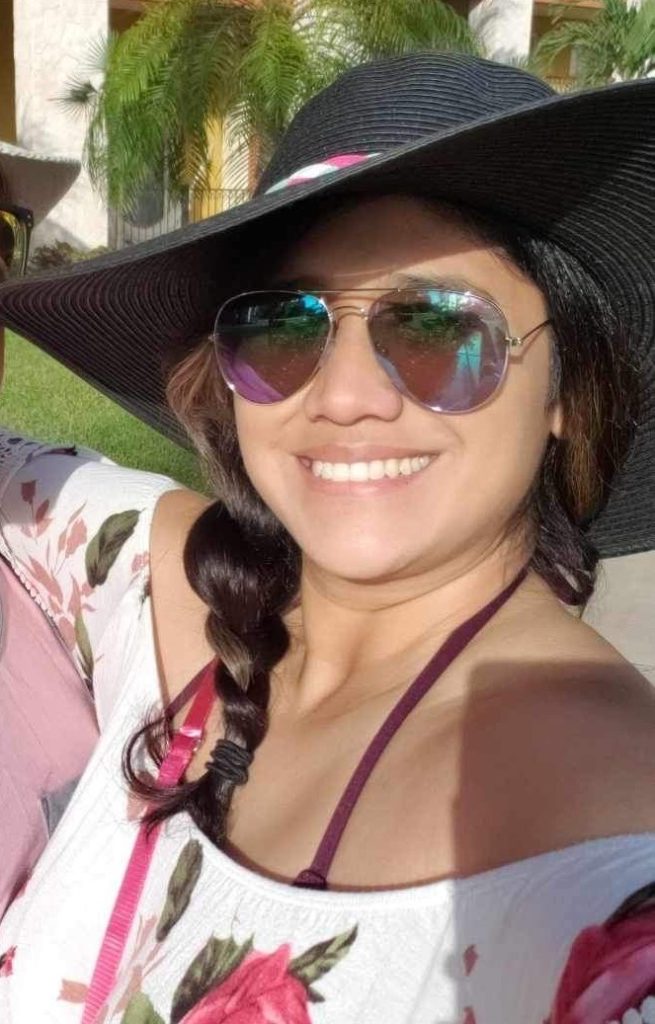 A woman wearing a hat and sunglasses is posing for a photo during her cruise. by Chasing the Sun Vacations