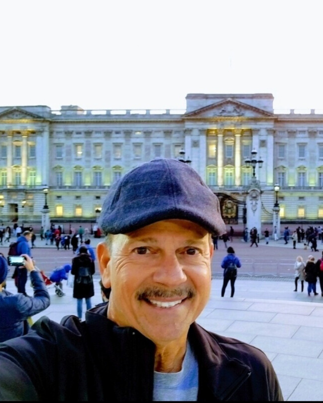 A man is taking a selfie in front of Buckingham Palace while on an all-inclusive vacation. by Chasing the Sun Vacations
