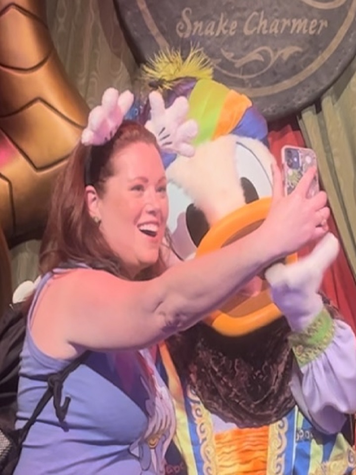 A woman taking a selfie with a donald duck mascot during her vacation, guided by a Travel Advisor. by Chasing the Sun Vacations