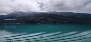 A blue lake surrounded by mountains under a cloudy sky. by Chasing the Sun Vacations