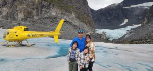 A group of people standing in front of a glacier with a helicopter in the background. by Chasing the Sun Vacations