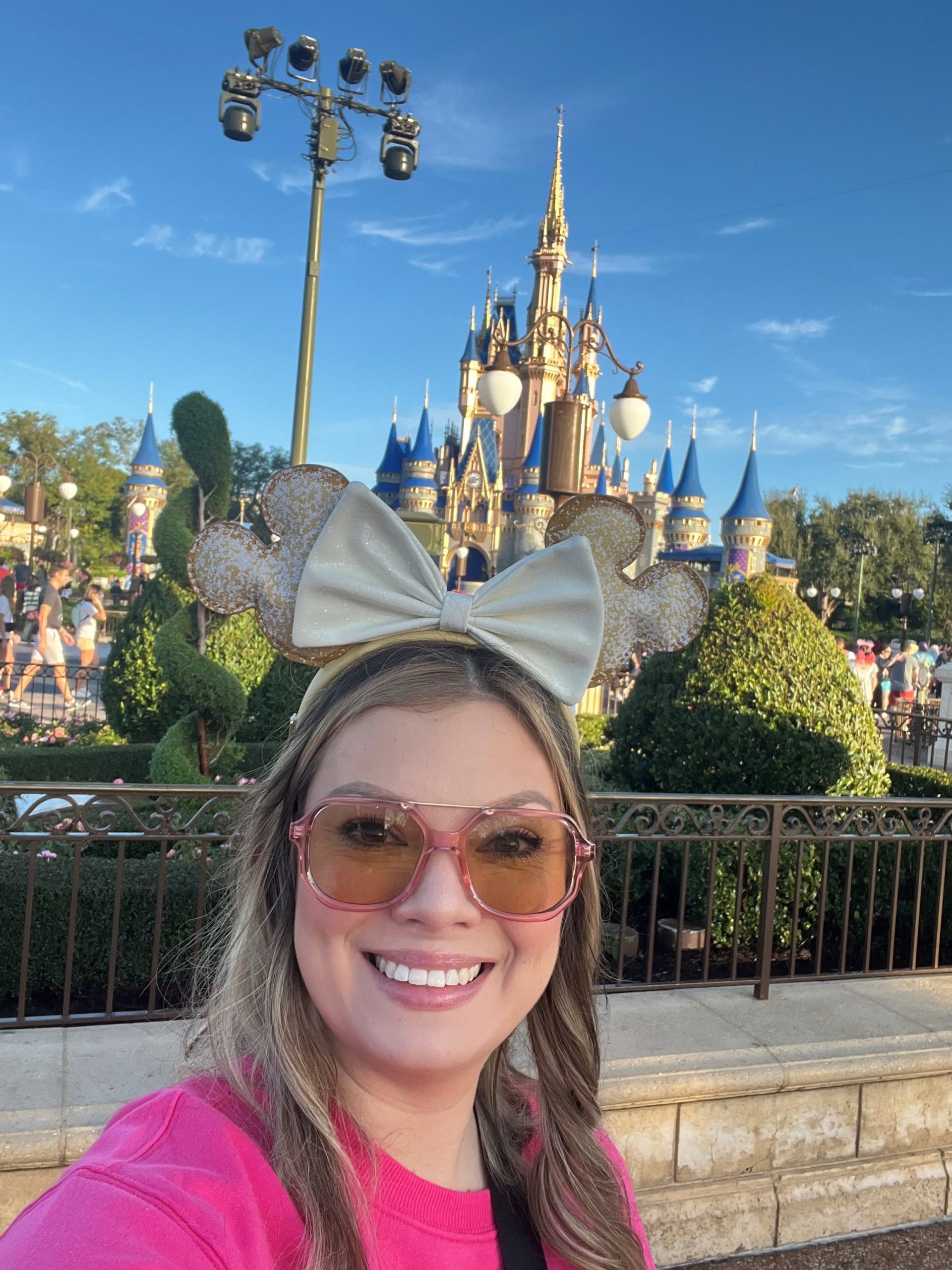 Woman wearing minnie mouse ears taking a selfie at disney with the castle in the background. by Chasing the Sun Vacations